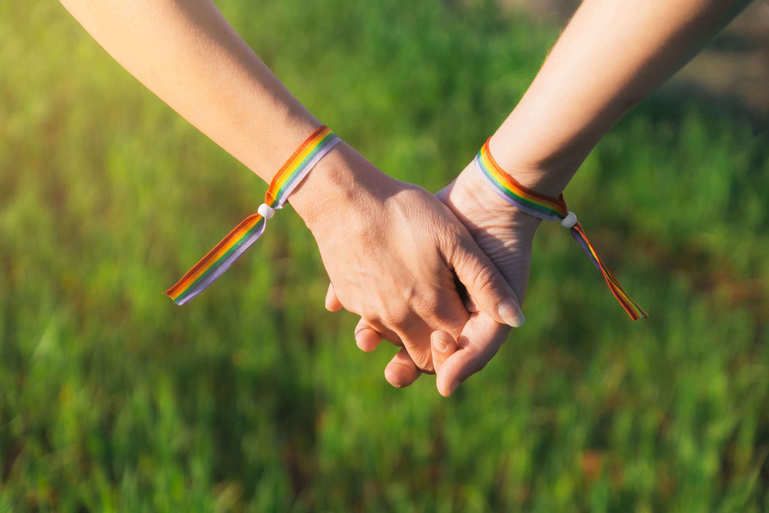 Two people holding hands with LGBT wristbands