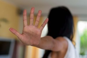A person extends their hand toward the camera with fingers spread, making a stop gesture. Their face is out of focus in the background, emphasizing the hand in the foreground.