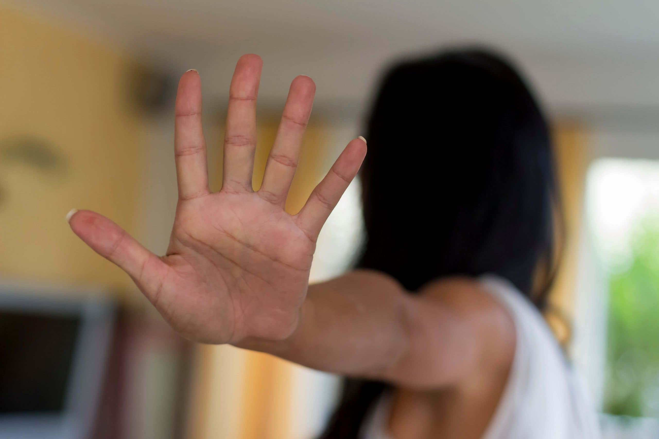 A person extends their hand toward the camera with fingers spread, making a stop gesture. Their face is out of focus in the background, emphasizing the hand in the foreground.