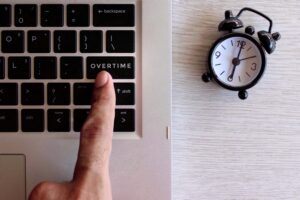 Blog header photo showing a person pressing an button that says overtime with a clock on the side