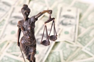 A bronze statue of Lady Justice holding scales stands in front of a scattered background of US dollar bills, symbolizing the work of an overtime attorney fighting for fair compensation.