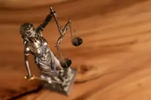 A bronze statue of Lady Justice holding balanced scales and a sword, symbolizing fairness like the Healthcare Whistleblower Protection Act, stands on a wooden surface. The statue is viewed from above, with emphasis on the scales.