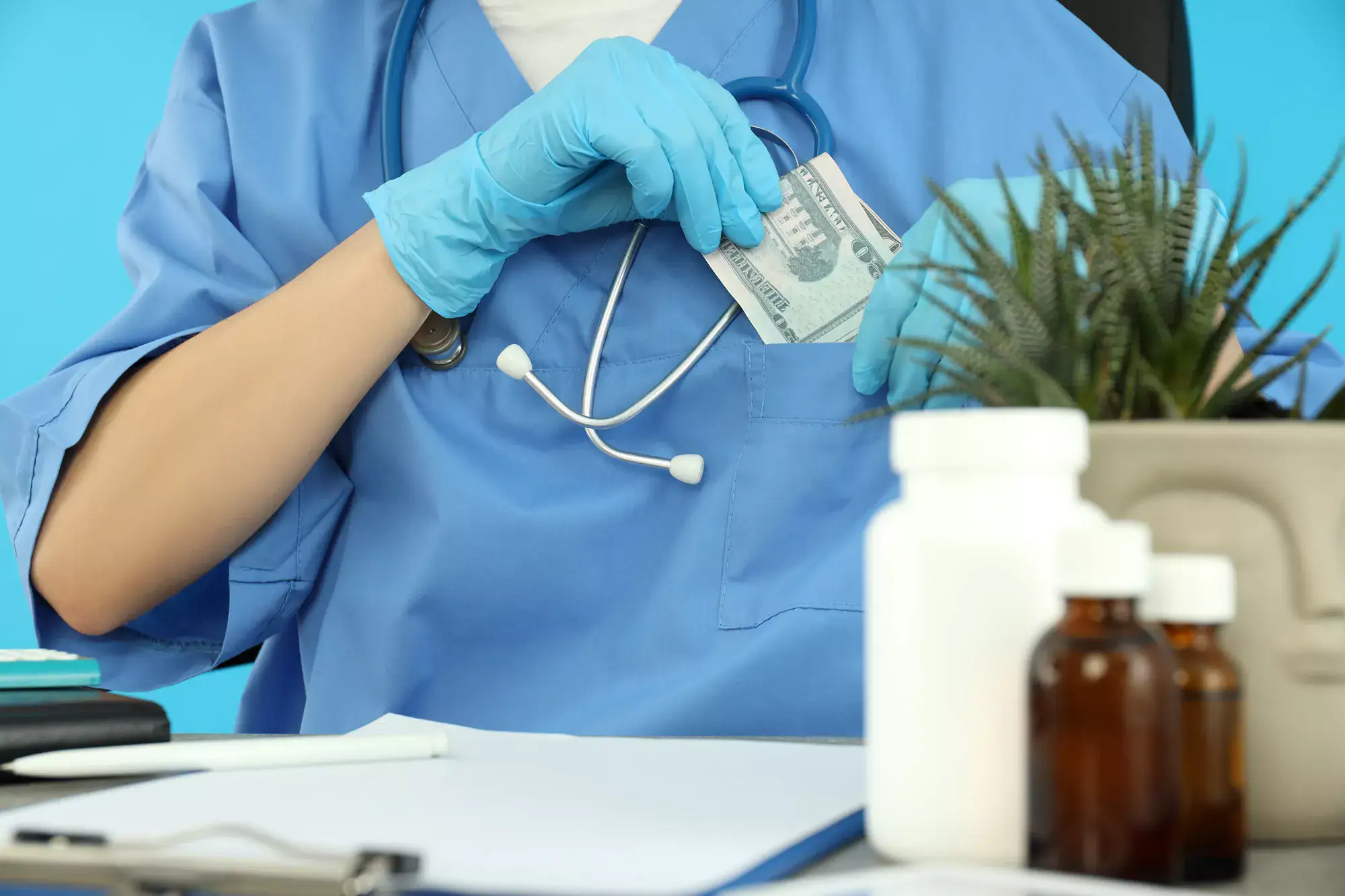A person in blue medical scrubs and gloves puts money into their chest pocket, with a stethoscope around their neck. On the desk are medicine bottles, a clipboard, and a potted plant—hinting at legal protection for whistleblowers in healthcare.