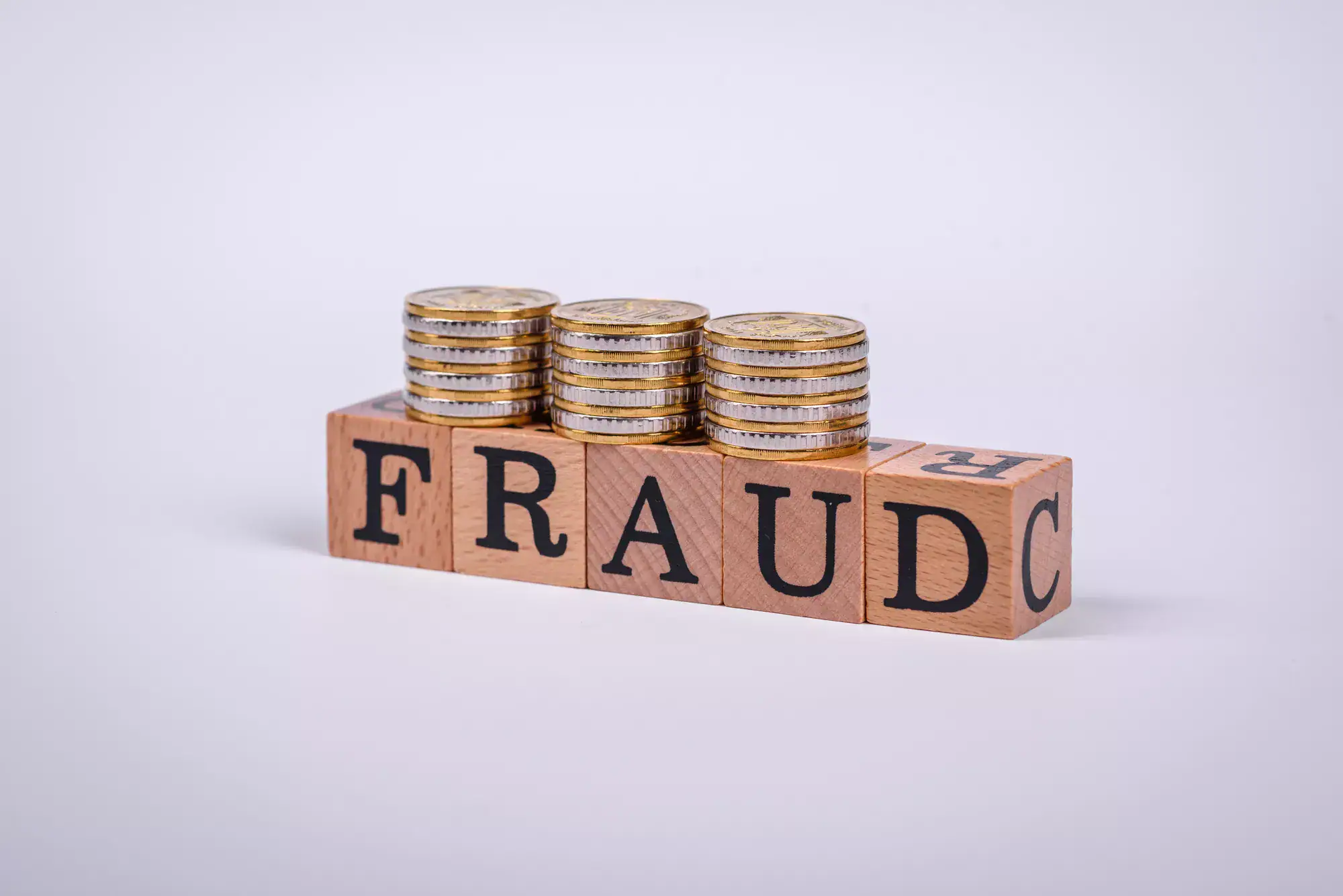 Four stacks of coins sit atop wooden blocks spelling "FRAUD" against a plain white background, symbolizing the potential healthcare fraud whistleblower reward.