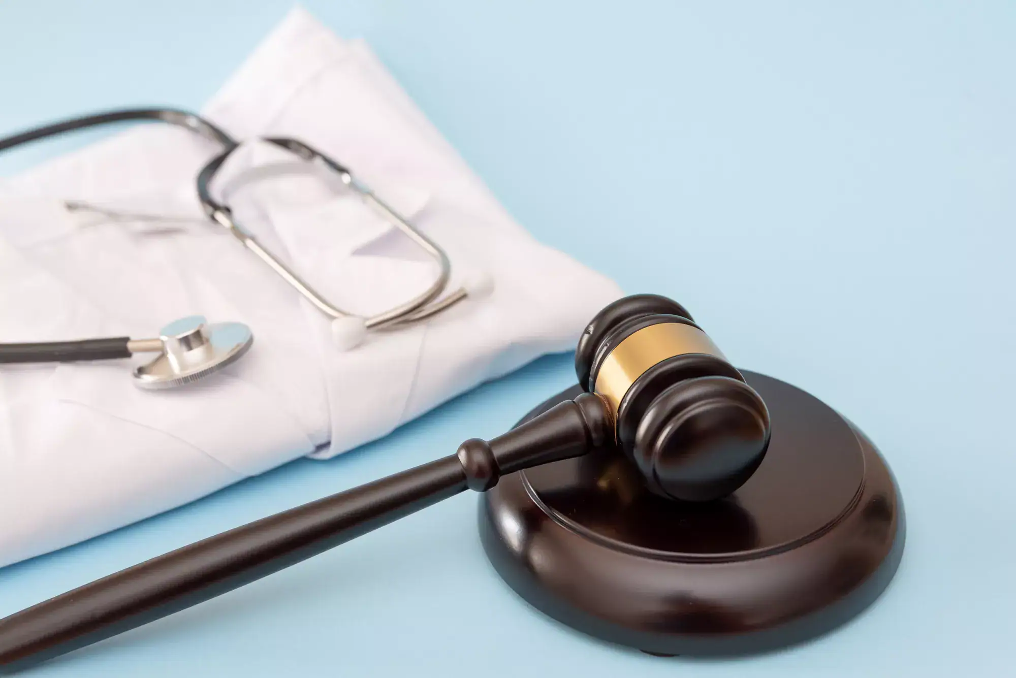 A judge's gavel rests on a sound block next to a folded white lab coat and stethoscope, symbolizing the intersection of law and medicine—raising questions like what is the Stark Law—on a light blue background.