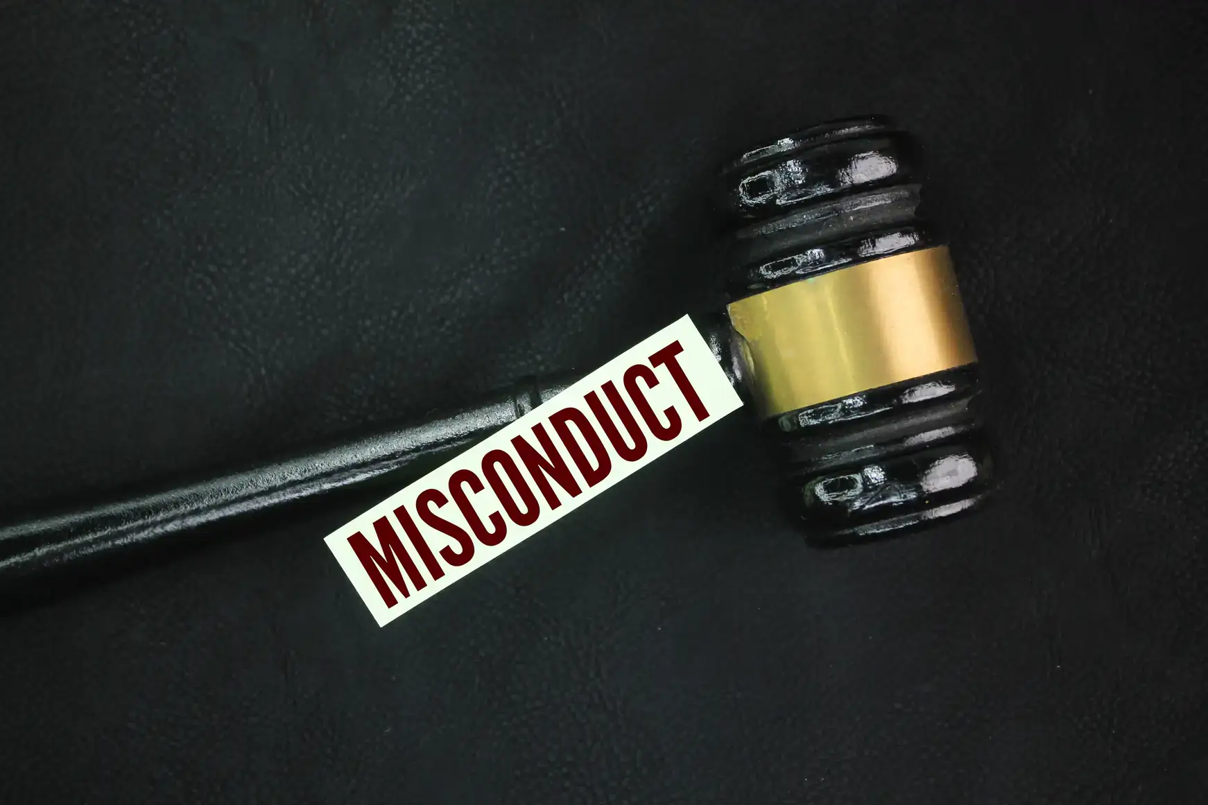 A judge&rsquo;s gavel rests on a dark surface with a white card labeled "MISCONDUCT" in bold red letters placed under the head of the gavel, evoking cases an NY sexual harassment attorney Manhattan might handle.