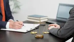 Two professionals in business attire sit at a desk with a scale of justice, open notebook, legal books, and a laptop, suggesting a consultation with a sexual harassment attorney in Manhattan, NY.