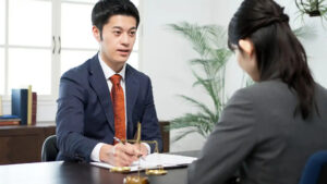 A lawyer in a suit consults with a client across a desk featuring a scale of justice.